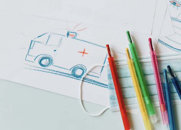 Child's drawing of an ambulance alongside colored pens and a face mask